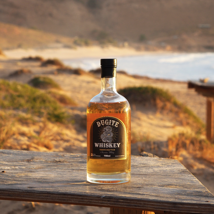 Dugite Whiskey 700ml bottle in a wooden bench in front of the ocean