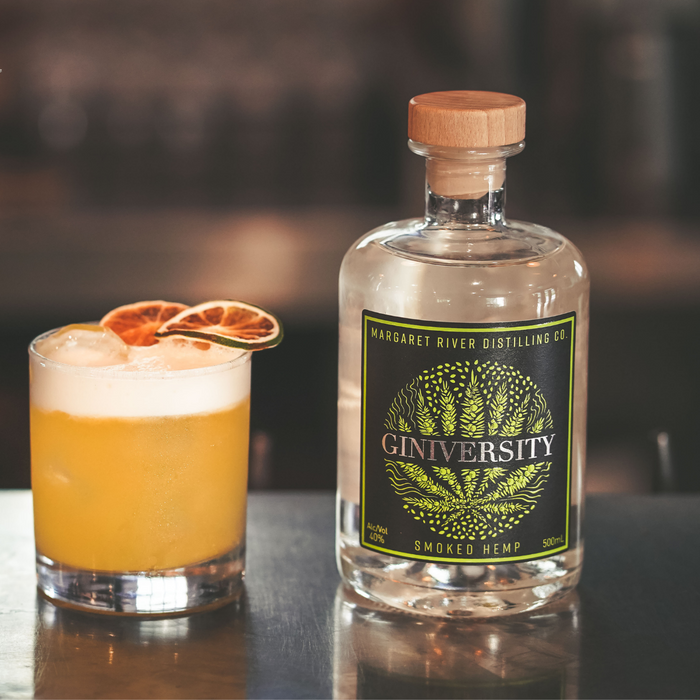 Giniversity Smoked Hemp 500ml bottle next to a cocktail with lime as a garnish