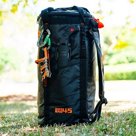 A black dry bag backpack with orange 'ROPE BAG 45' text, standing upright on grass outdoors with a blurred natural background.